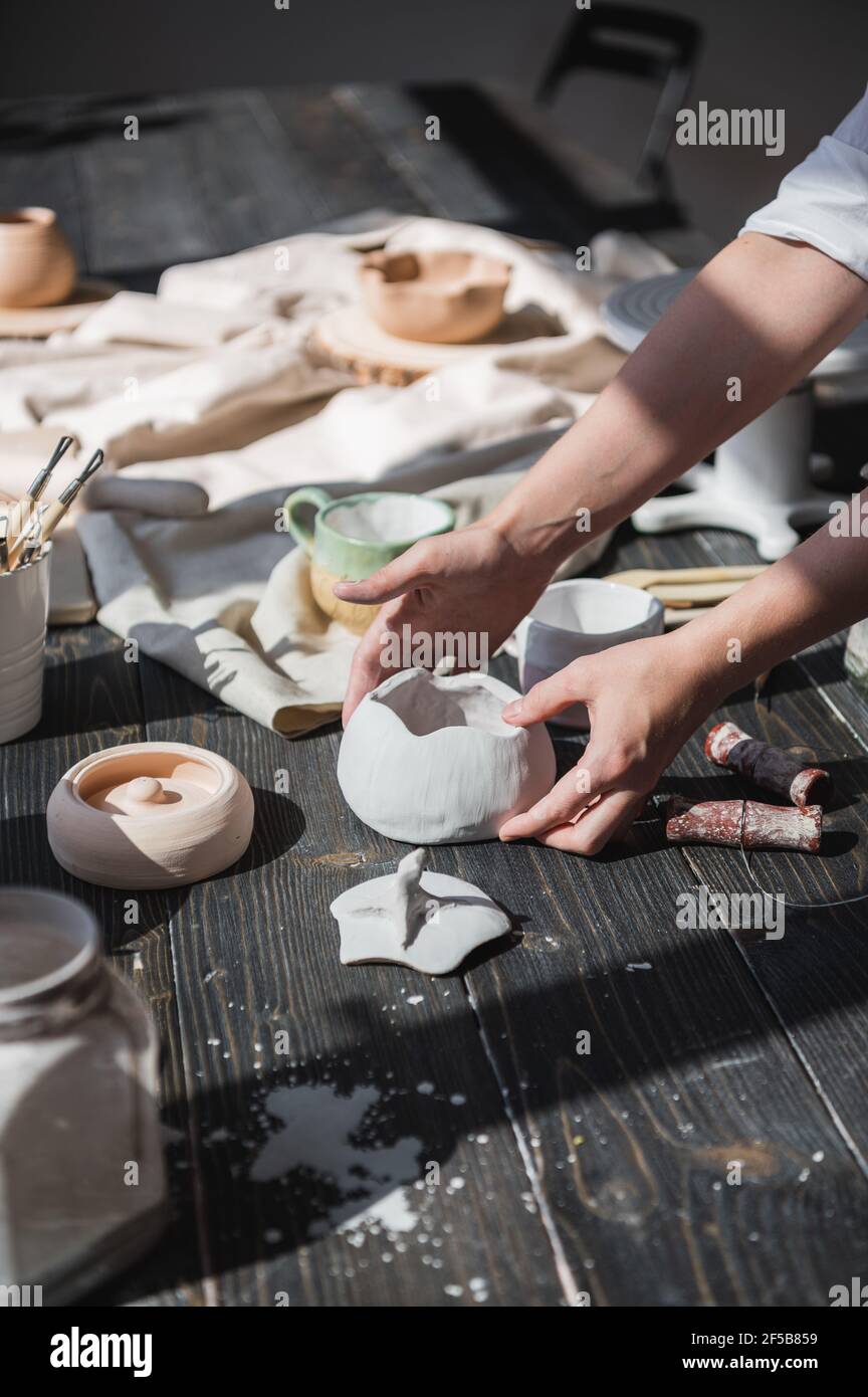 Female hands gently putting the finished glazed bowl on a wooden table with different pottery tools Stock Photo