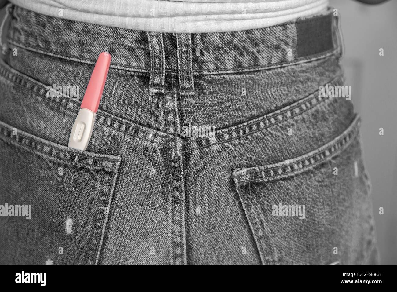 Young woman with positive pregnancy test in pocket of jeans close-up black and white Stock Photo