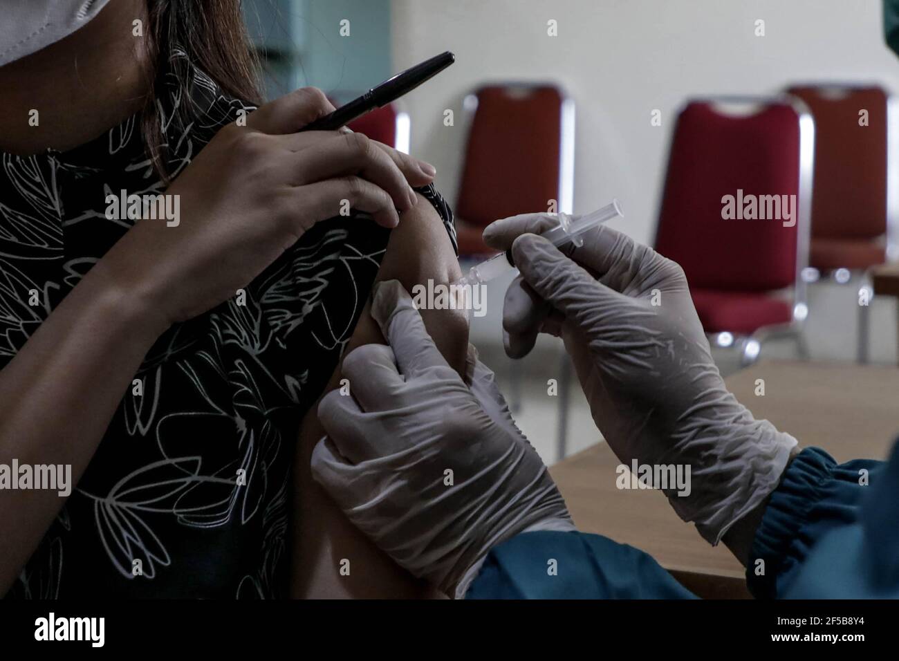 A healthcare worker injects a dose of Sinovac COVID-19 vaccine to a worker during a mass vaccination drive for the public sector workers at Geospatial Information Agency Office in Bogor.Indonesia is currently in the second phase of mass covid-19 vaccination. In this second phase, the Indonesian government targets 38.5 million people, including 16.9 million workers in public sectors and 21.6 million elderly citizens, as well as workers in hospitality, transportation, tourism sectors and mass media workers. Stock Photo