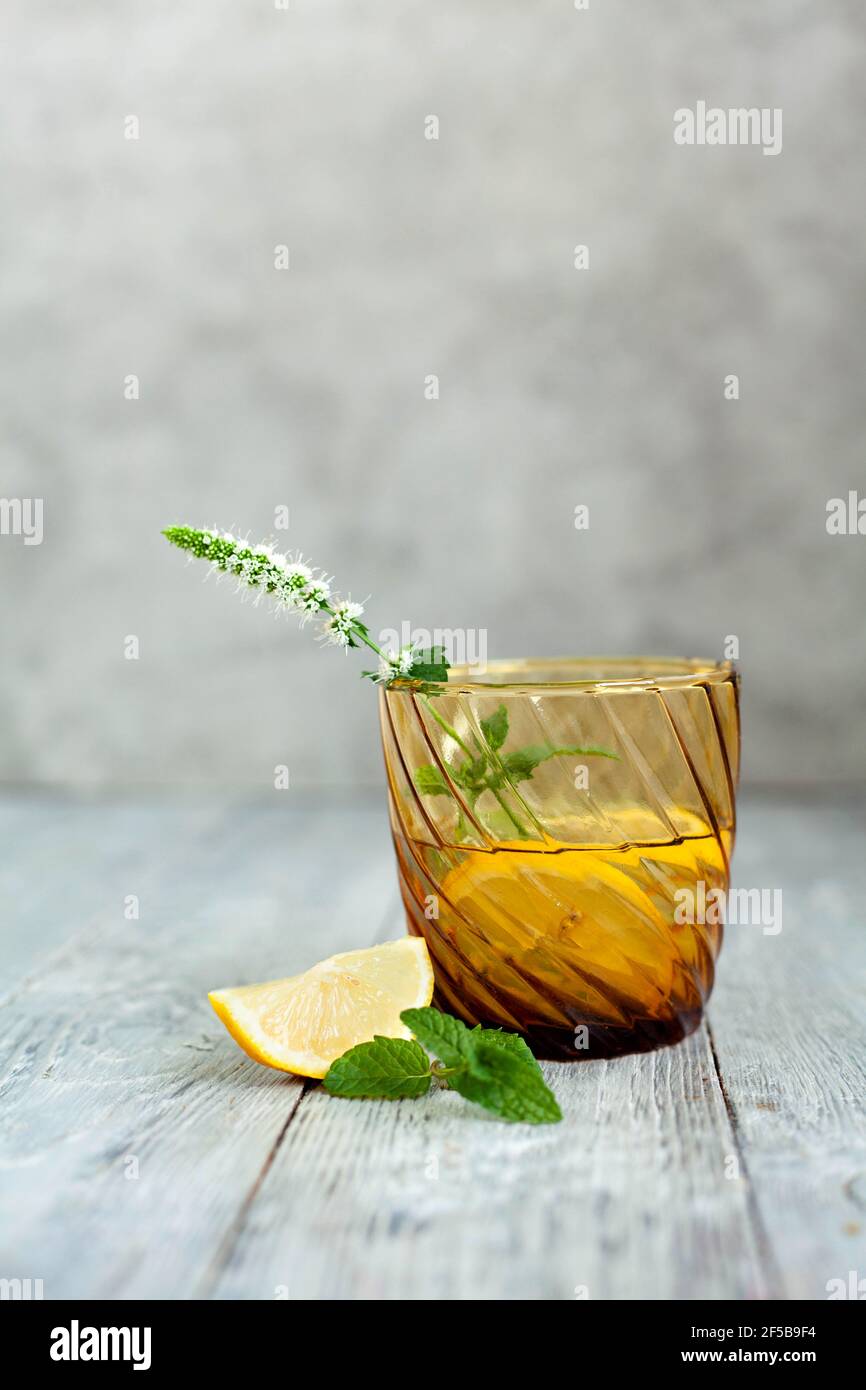 One yellow stylish glass with a refreshing cocktail with lemon and mint on a gray textured background or table. Copy space and summer drink for menu. Stock Photo