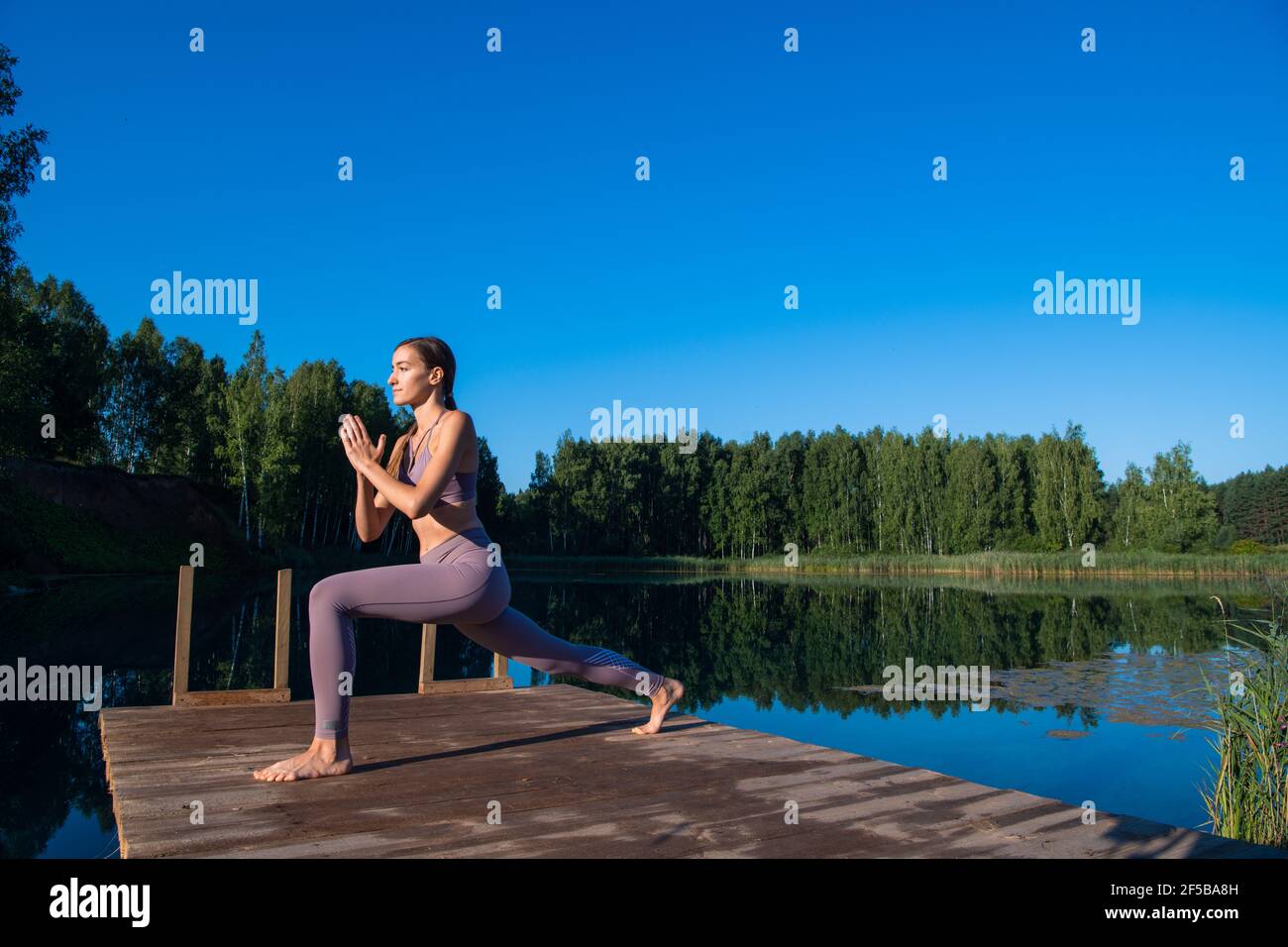 Young female practicing yoga against the sky on a sunrise. Pretty slim woman performs an exercise. Healthcare, meditaion, welness, mindfulness concept Stock Photo