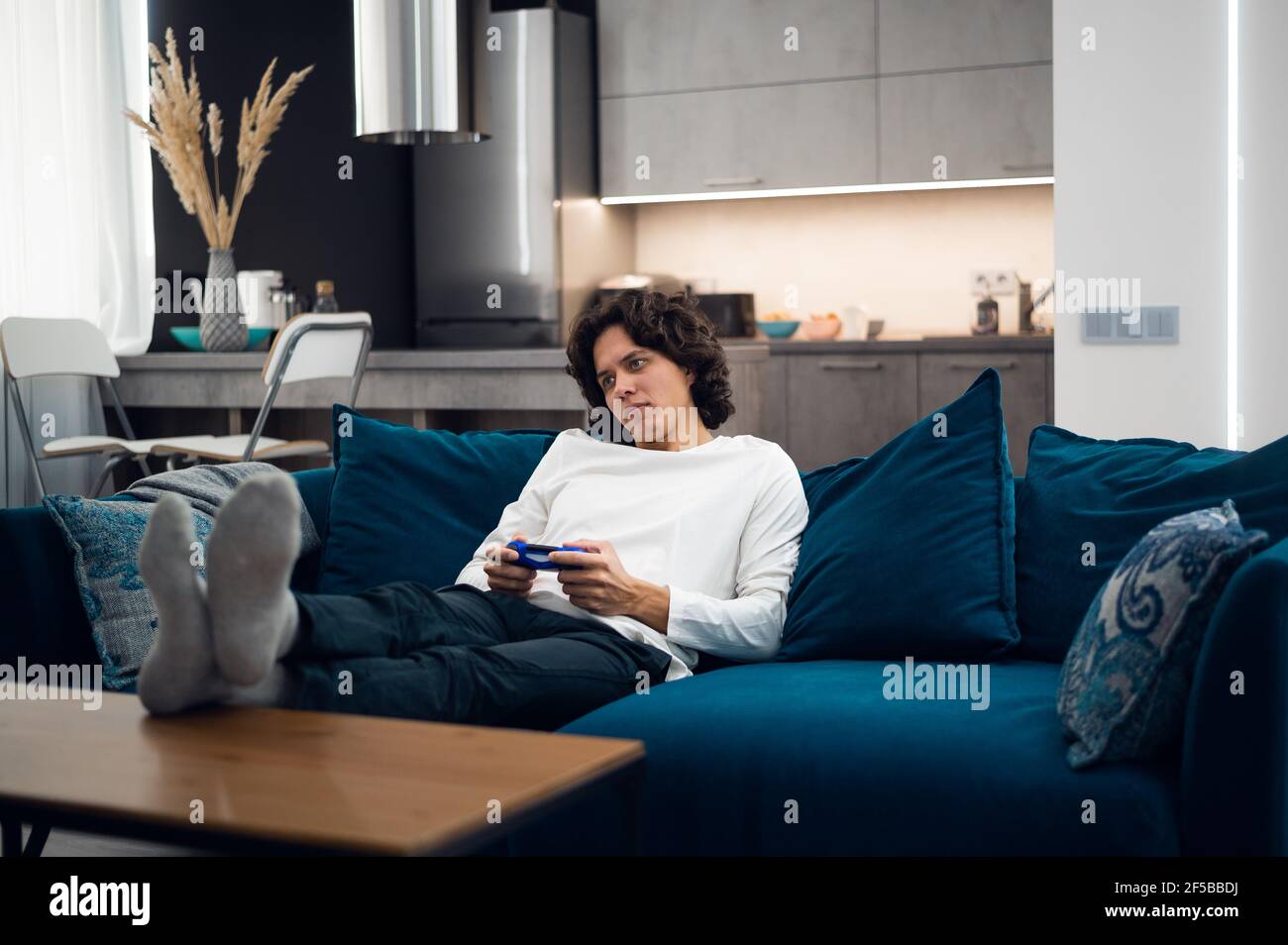 Bored young man playing video game while lying on sofa at home. Stock Photo