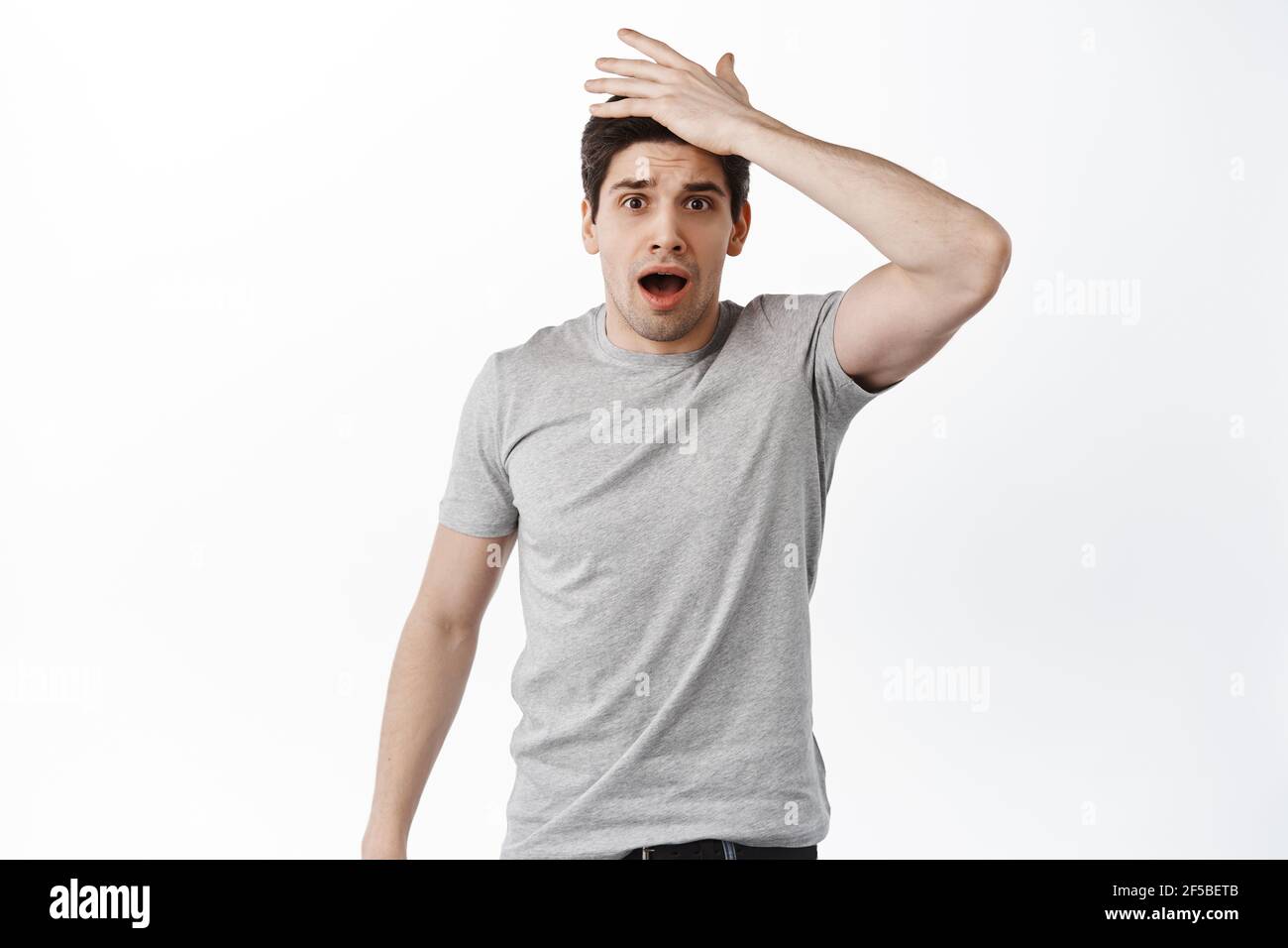 Shocked man forgot remember something, slap forehead and gasp at camera, standing forgetful against white background Stock Photo