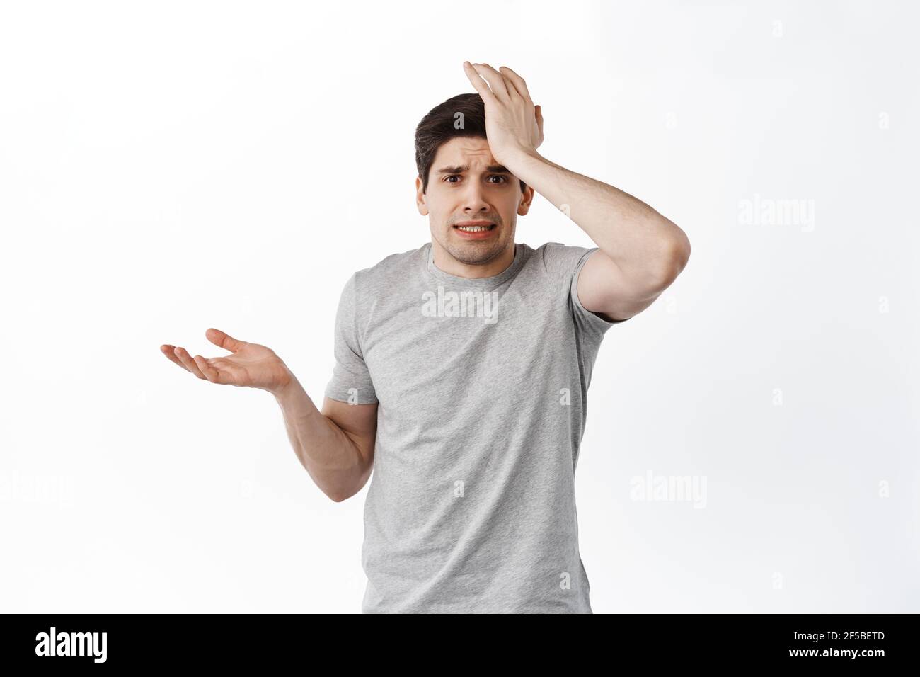 Nervous man look confused and worried, slap forehead and shrugging, forgot remember, made mistake, standing distressed against white background Stock Photo