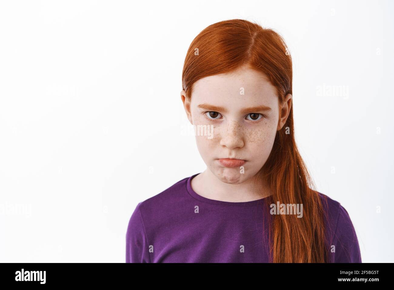 Close up of sad redhead girl with freckles sulking, angry or gloomy looking at camera, being upset or jealous, frowning dipleased, standing over white Stock Photo