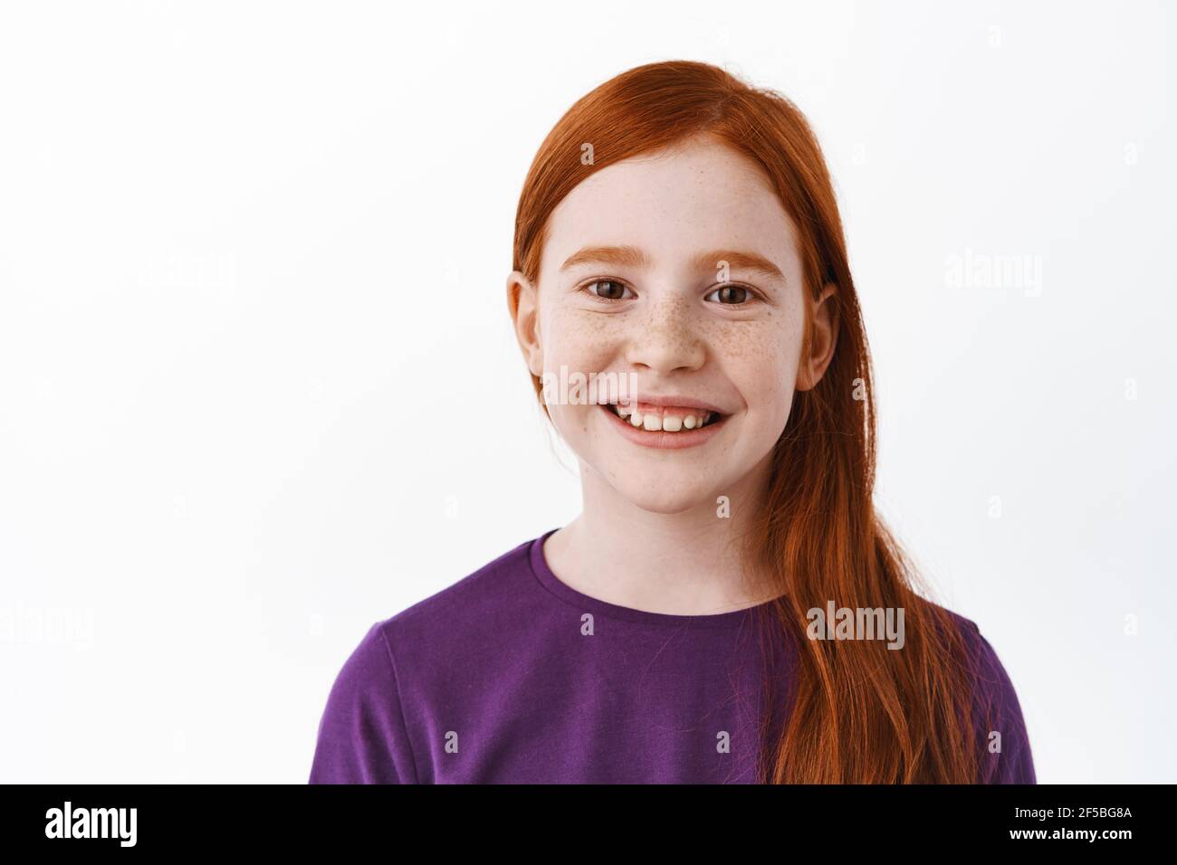 Close up portrait of beautiful red haired girl with freckles, smiling with teeth and looking happy at camera, positive emotion, joyful kid, white Stock Photo