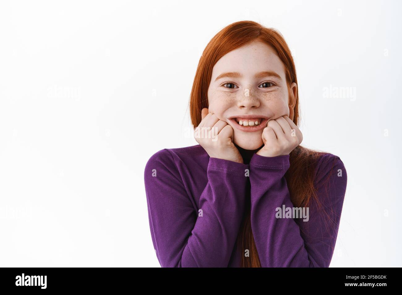 Portrait of beautiful redhead child, little ginger girl with freckles touch cheeks and smiling