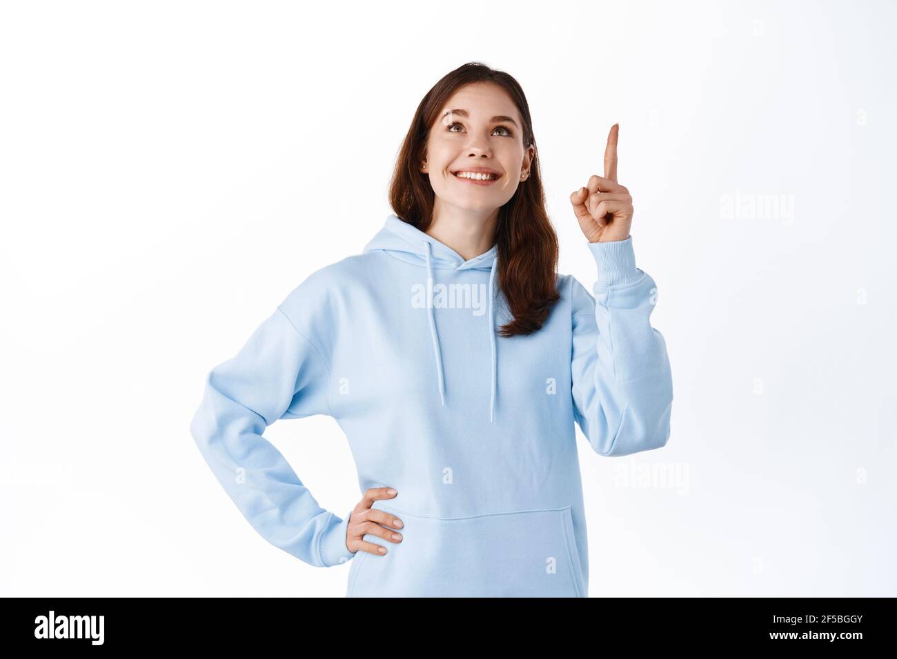 Girl in blue hoodie pointing and looking up at promo logo, smiling pleased, showing good
