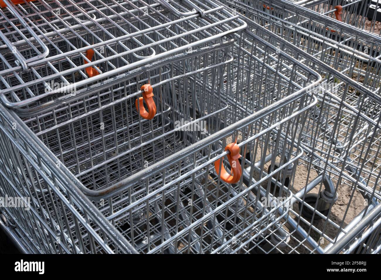 A row of empty shopping carts with orange plastic grocery bag hooks