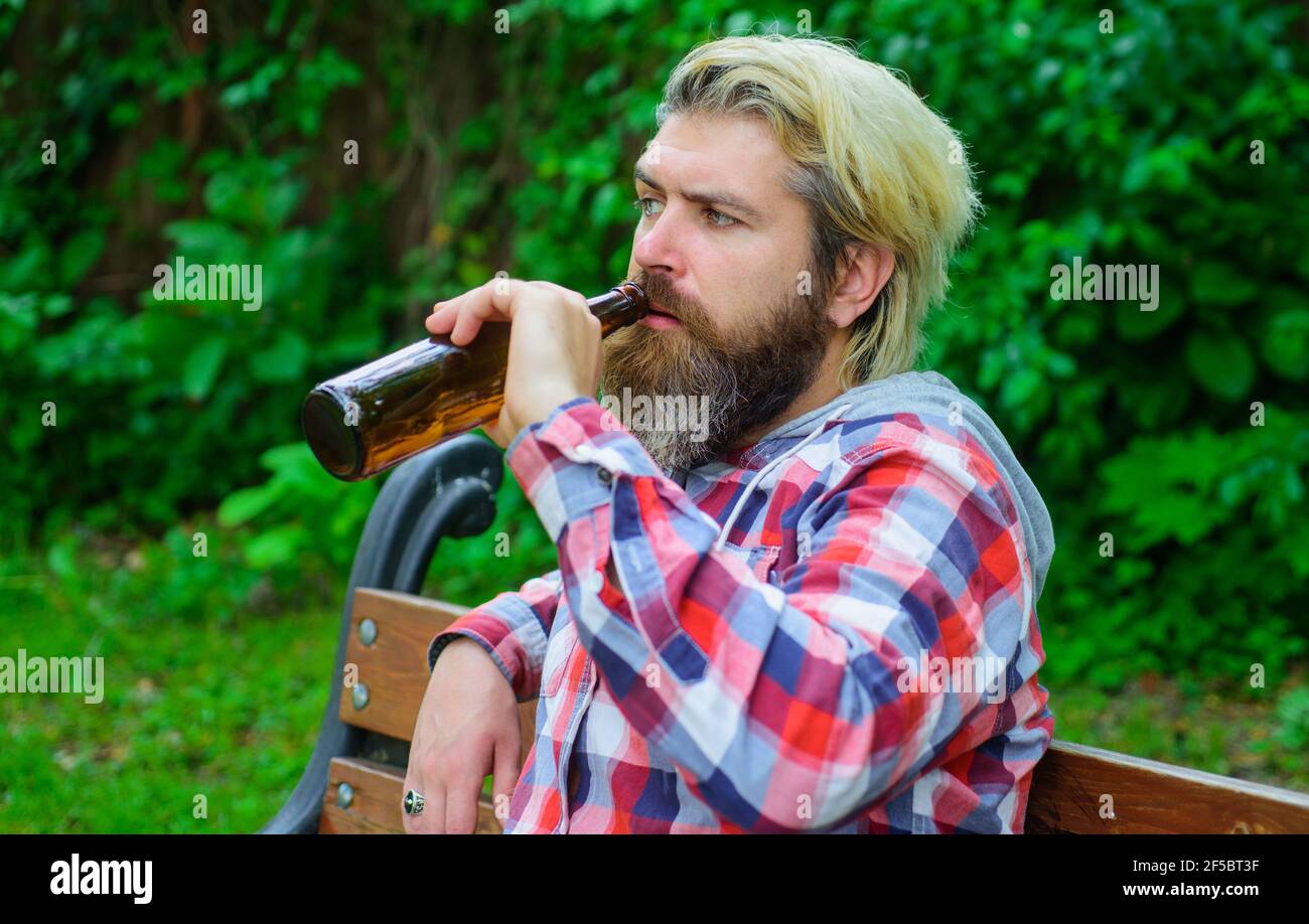 Handsome man drinks bottled beer. Bearded male in casual clothes enjoying beer in summer. Stock Photo