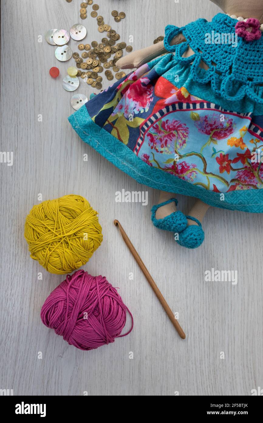 Brown sewing needle and yarn balls next to a handcrafted multicolor doll over a wooden gray background. Stock Photo