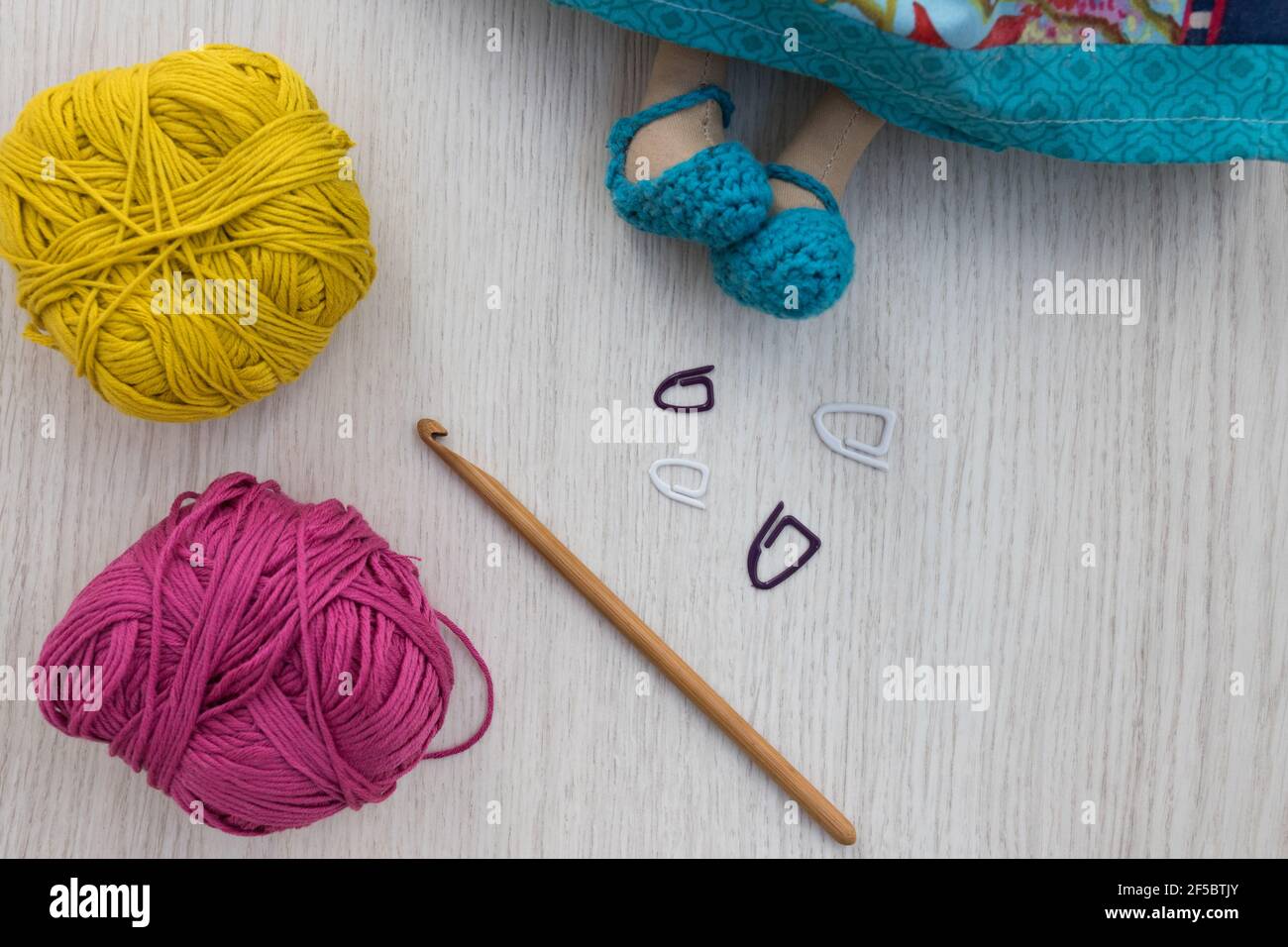 Four clips, a brown sewing needle and two yarn balls next to the lower part of a handcrafted multicolor doll. Stock Photo