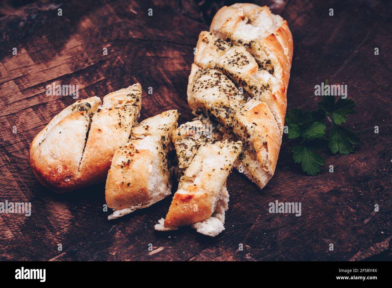 Tasty bread with garlic, butter and herbs on old wooden table Stock Photo