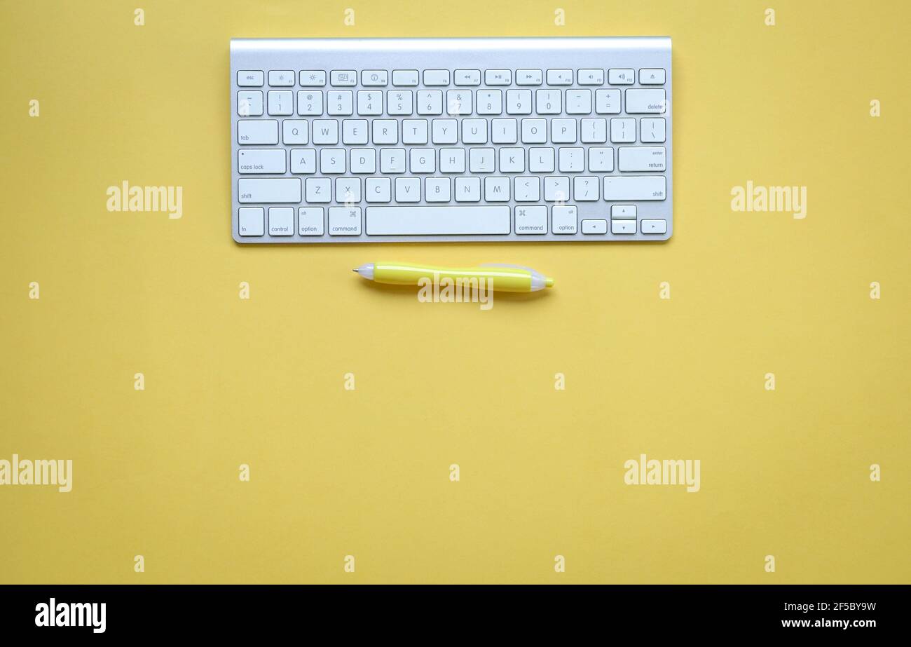 Yellow office desk with computer keyboard and yellow pen. Top view