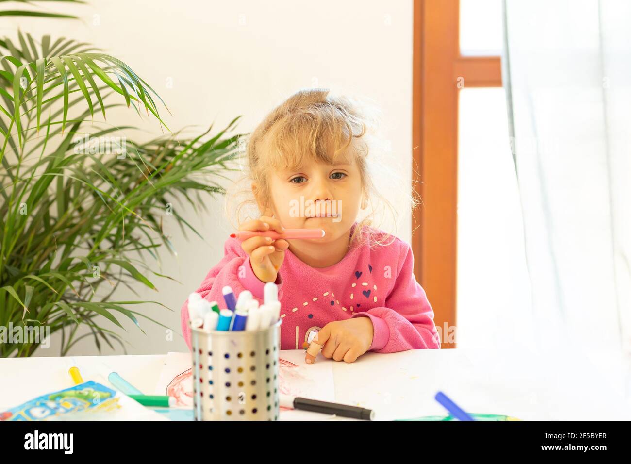 Under quarantine fun. Little girl painting during coronavirus outbreak and doing homework. Lifestyle under corona virus. Stock Photo