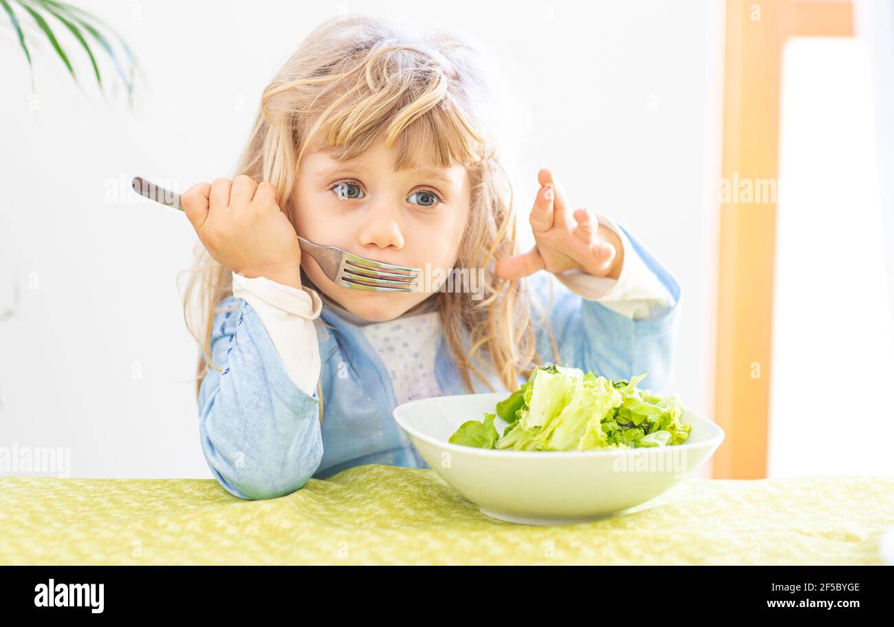 Small blonde girl refusing to eat vegetable salad. Lifestyle Concept Stock Photo