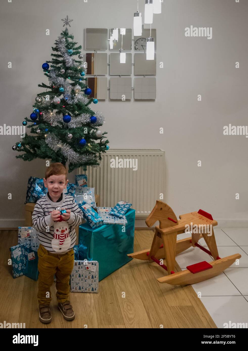 A cute, redhead, blue-eyed baby boy in front of a Christmas tree holdin a blue bauble Stock Photo