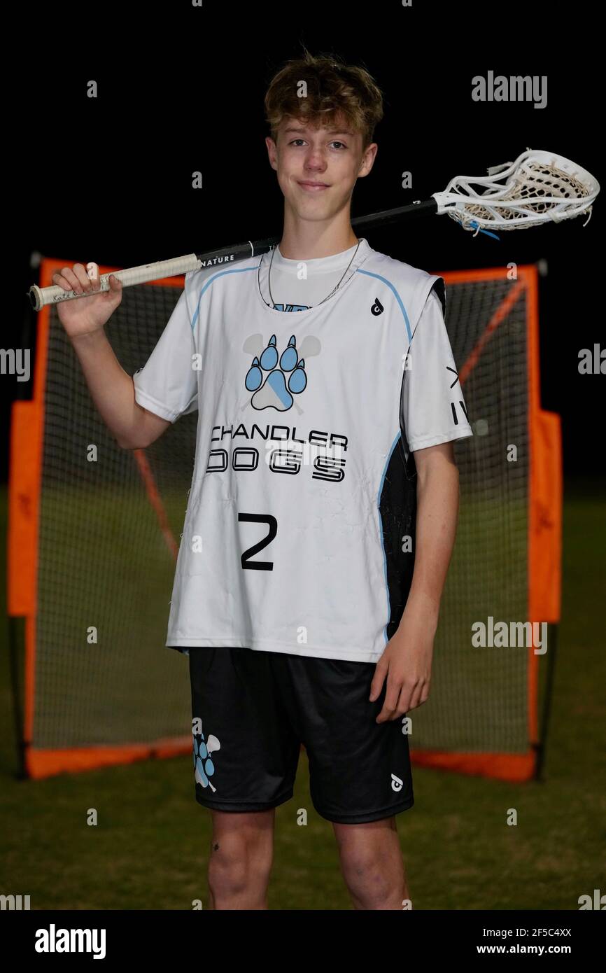 A teenage boy poses for a portrait in his lacrosse sports uniform in front of a goal. Stock Photo