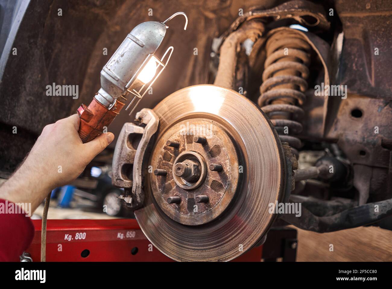 A car mechanic inspects brake discs and pads with a flashlight. Car on a repair stand. Technical service station for car. Stock Photo