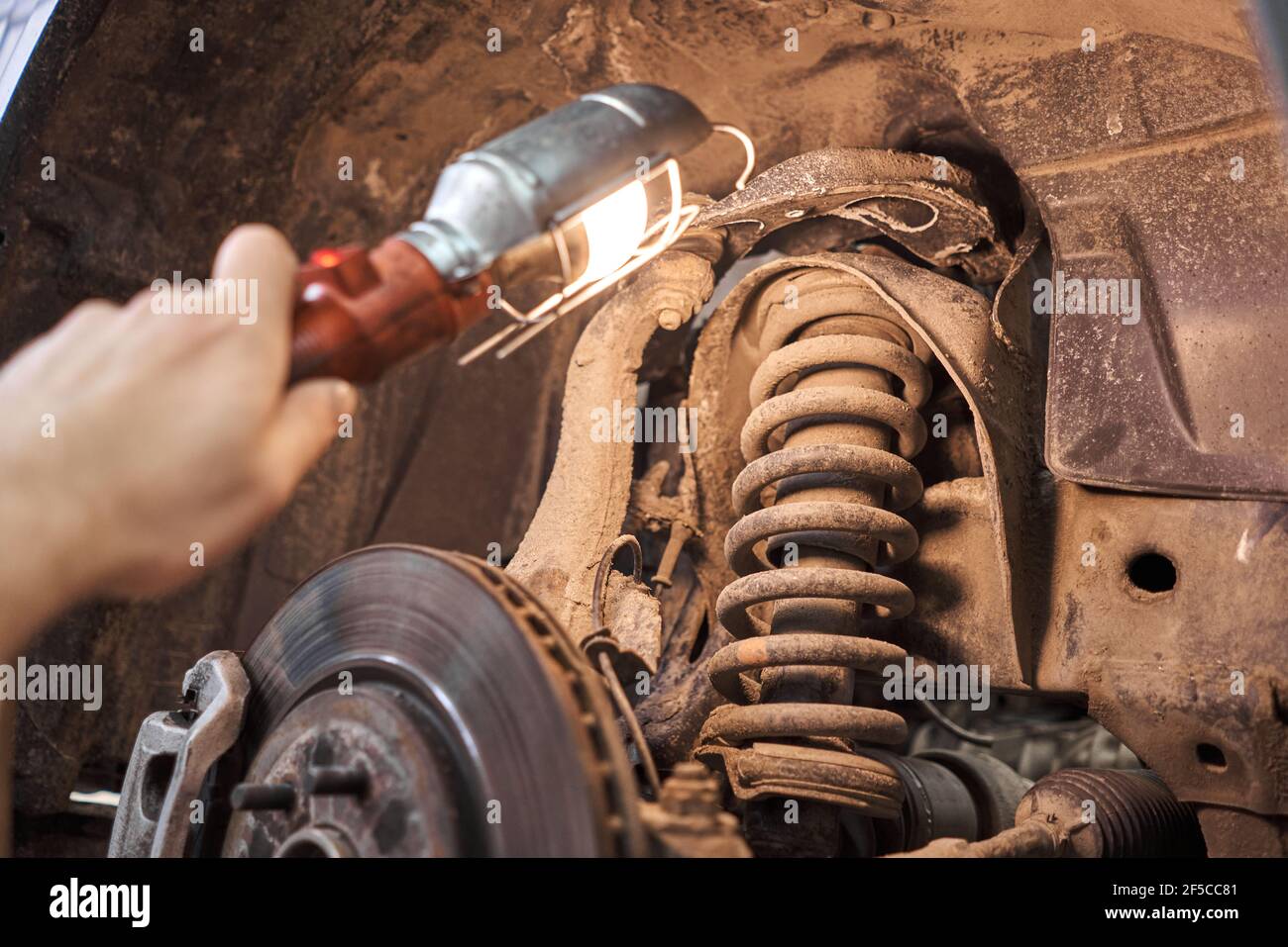 A car mechanic inspects shock absorber, springs and stabilizer bars with a flashlight. Car on a repair stand. Technical service station for car. Stock Photo