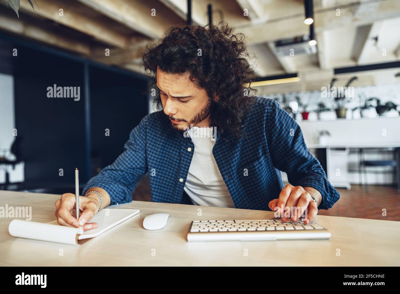 Handsome curly guy is making notes at the working table in open space office Stock Photo