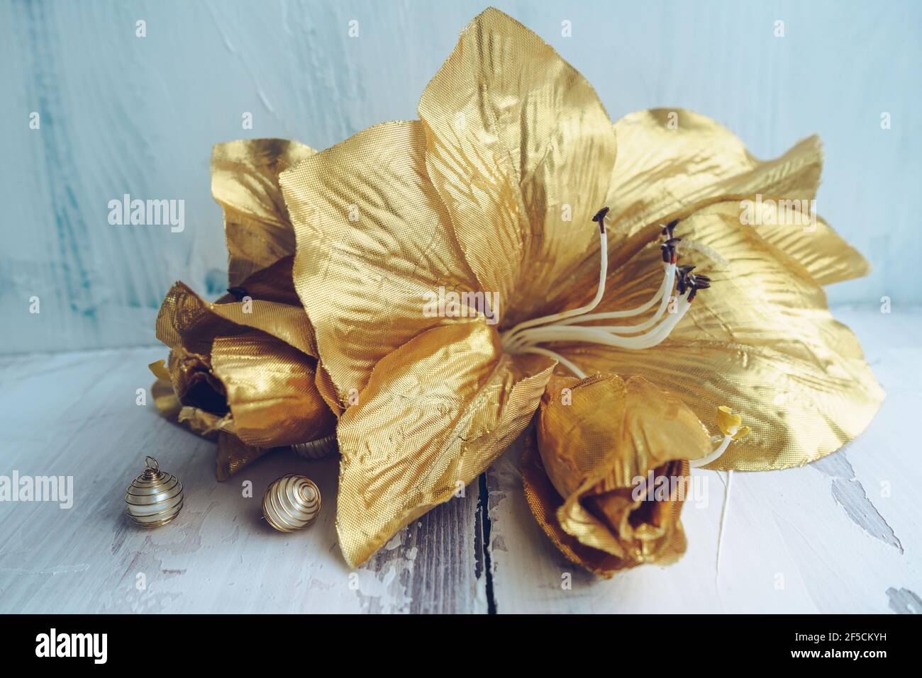 artificial golden lily flowers and beads with light wooden background Stock Photo