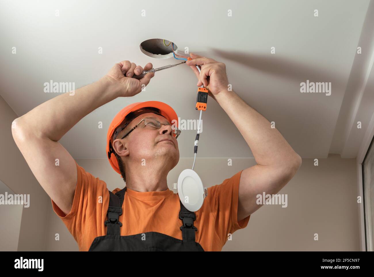 The electrician is installing an LED spotlight in the ceiling Stock Photo -  Alamy