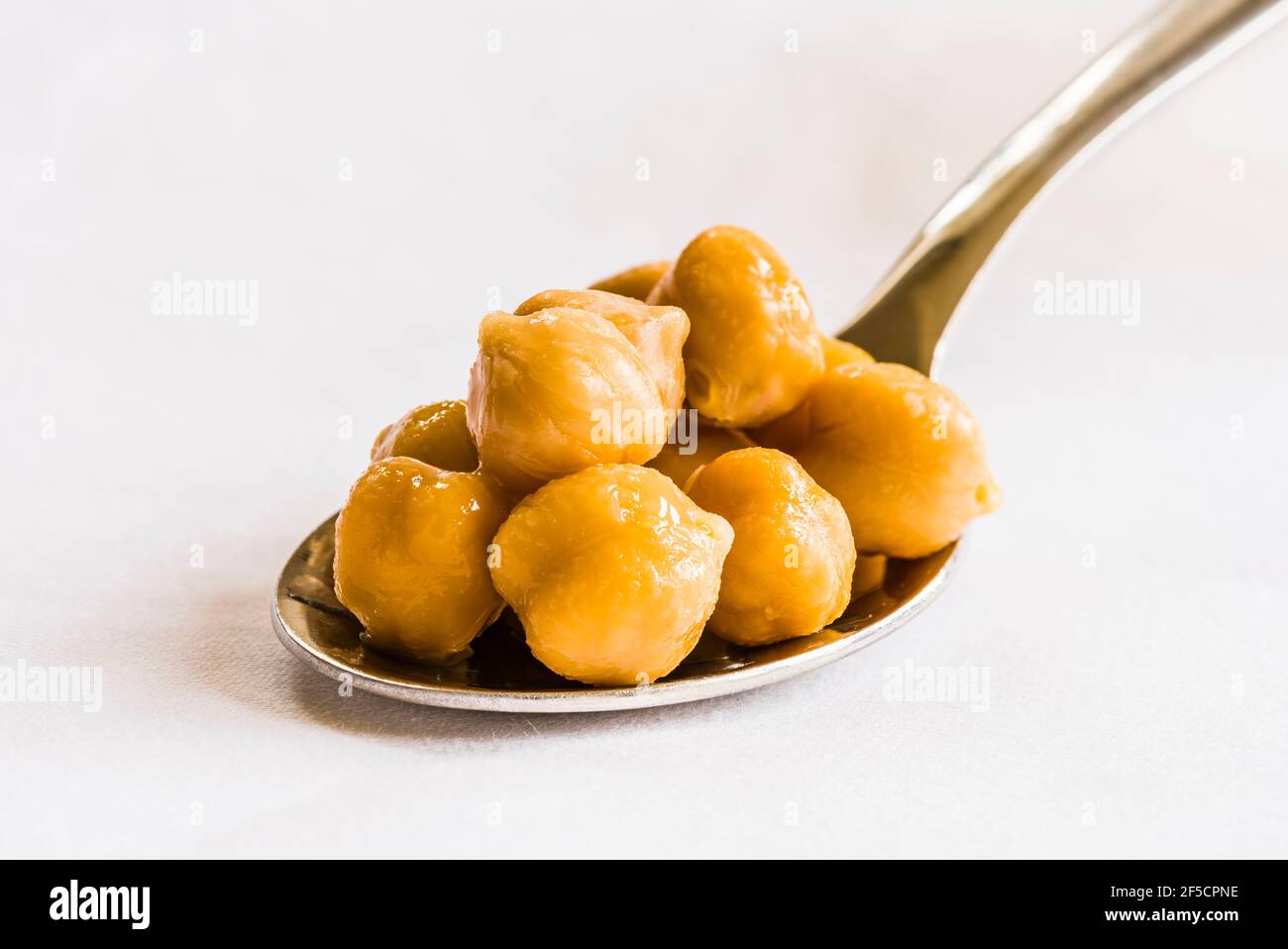Close-up of chickpeas on a silver spoon on a white tablecloth, London, UK Stock Photo