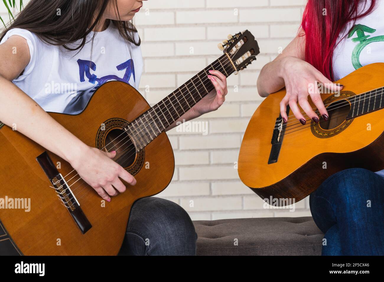 Anonymous girlfriends in t shirts with transgender symbol sitting on bench and playing Spanish guitars together Stock Photo
