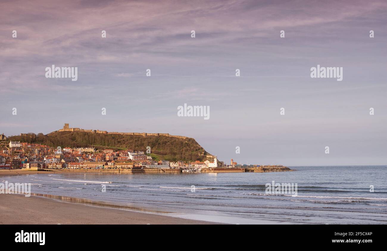 Panoramic view of a seaside town. The buildings of the town is are lit be a fading sun and the ruins of a castle stand on top of a hill. Stock Photo