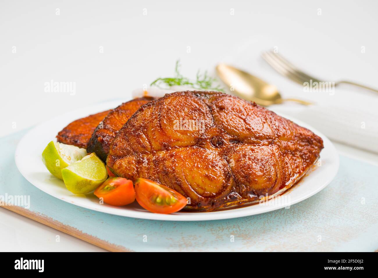 Seer fish fry arranged beautifully and garnished with onion, lemon and tomato slices on white ceramic plate placed on sky blue board with white textur Stock Photo