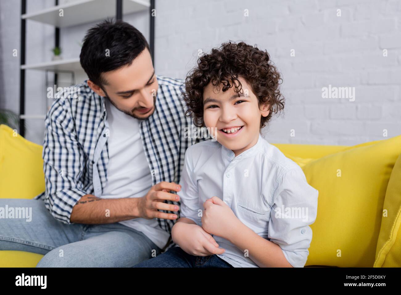cheerful arabian man tickling joyful son while sitting on sofa at home Stock Photo