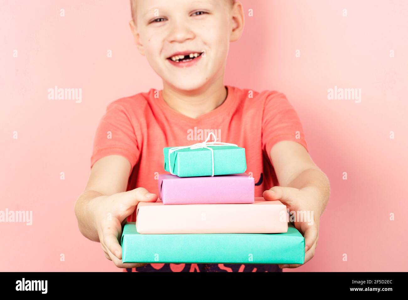 Smiling boy holding four gift boxes in pastel color. Stock Photo