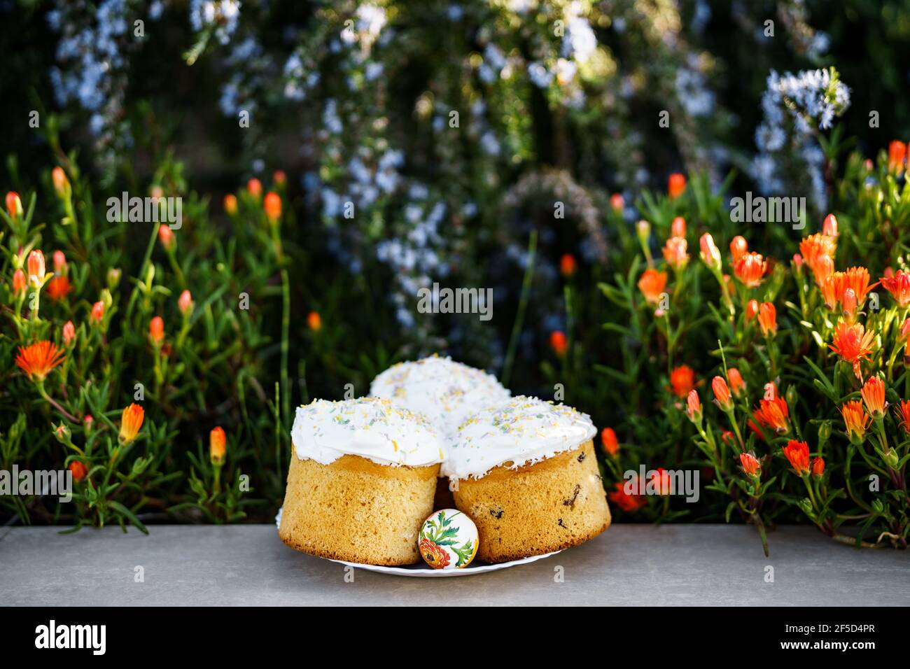 Plate with three Easter cakes covered with white glaze, in a flower bed. Stock Photo