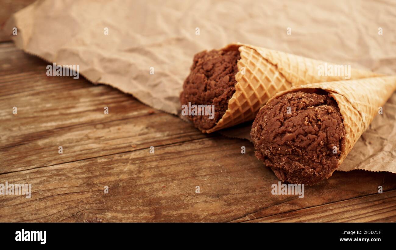 Chocolate ice cream in a waffle cone on craft paper on a wooden ...