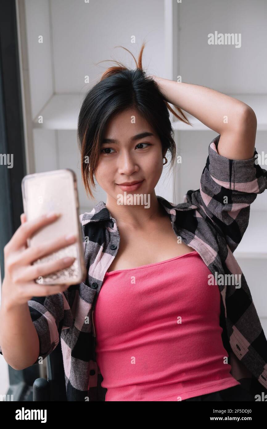 Image of young brunette asian woman smiling and taking selfie photo on cellphone at cafe shop Stock Photo