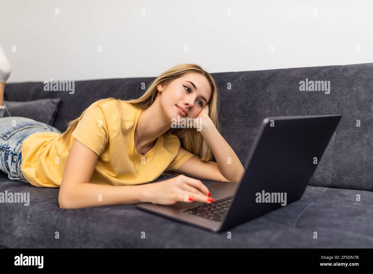 Casual young woman lying on couch and using laptop at home. Working ...