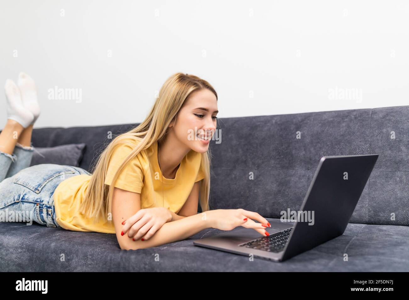 Casual young woman lying on couch and using laptop at home. Working ...