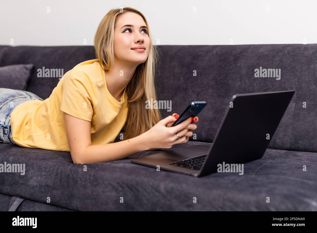 Smiling woman sitting on sofa at home with computer, shopping in internet, making purchases in online store, entering payment confirmation code from m Stock Photo