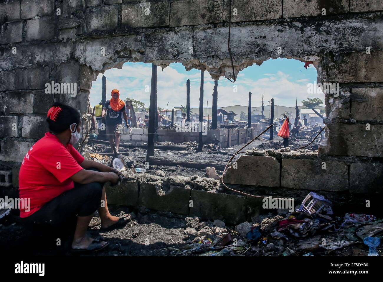 Rizal Province. 26th Mar, 2021. A woman looks through a large hole on a concrete wall as she rests from searching for her belongings from charred home after a fire at a slum area in Rizal Province, the Philippines on March 26, 2021. The Philippine Bureau of Fire Protection said that the fire is believed to have started from one of the houses that was being used as a garment manufacturing area, leaving more than 170 families homeless in the fire. Credit: Rouelle Umali/Xinhua/Alamy Live News Stock Photo