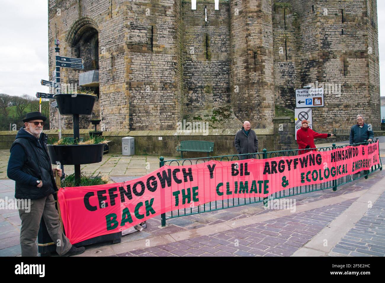 Caernarfon, Gwynedd, North Wales, UK. 26th March 2021. Members of Extinction Rebellion North Wales joined by Plaid Cymru MP Hywel Williams hold a banner calling for the backing of the Climate and Ecological Emergency bill outside Caernarfon Castleas part of a national banner drop day of action.Parliament declared a Climate Emergency back in 2019 – but protestors say actions haven’t matched their words. An emergency requires strong, decisive action to reverse the climate and ecological crisis. Stock Photo