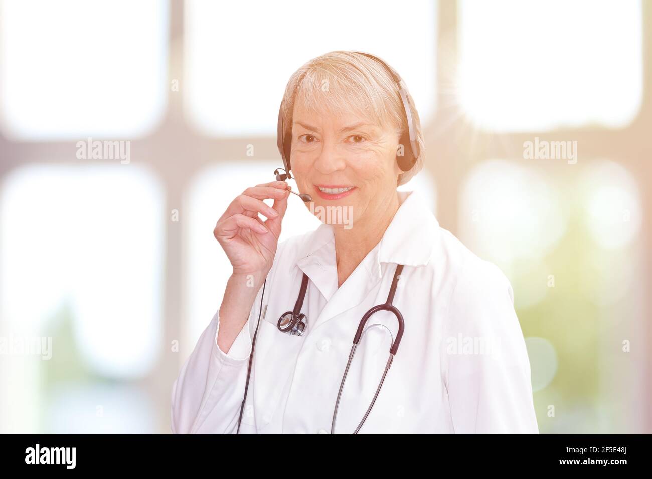 Friendly senior doctor during an online consultation as seen through a webcam, light background. Stock Photo