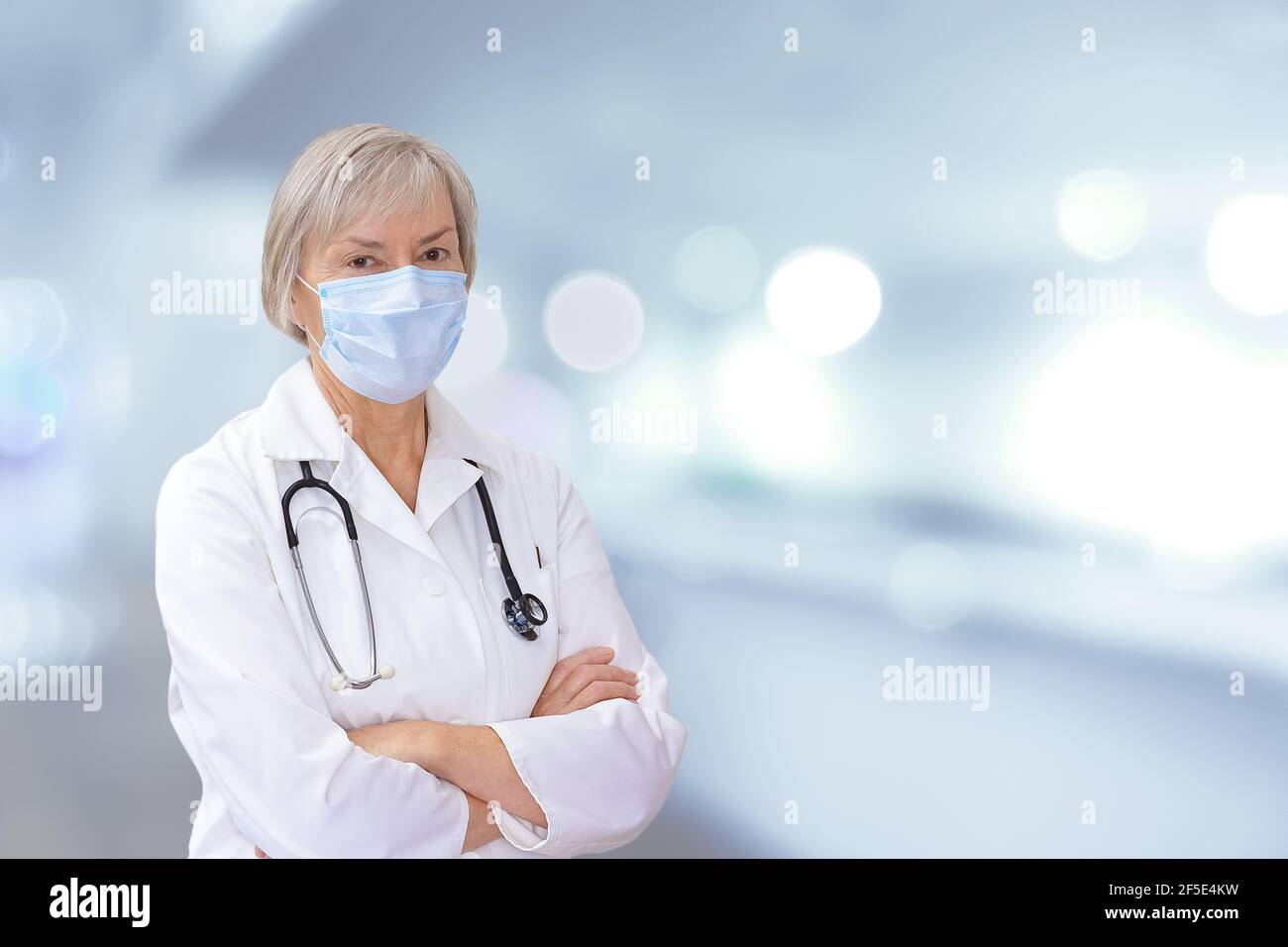 Senior female doctor with protective face mask, blurred background, copy or text space. Stock Photo