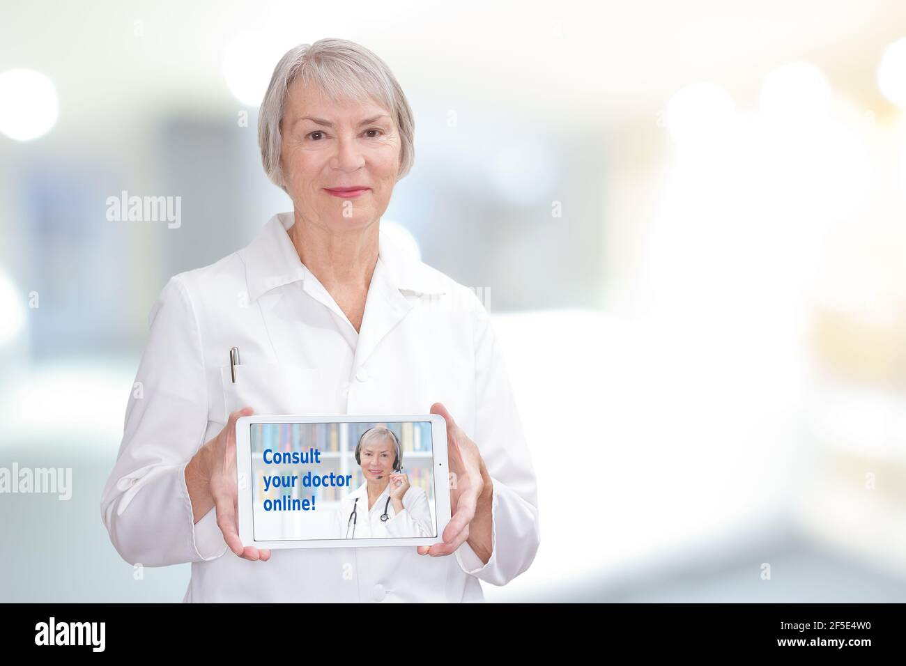 Friendly senior doctor showing a tablet computer with the text: consult your doctor online, copy space. Stock Photo