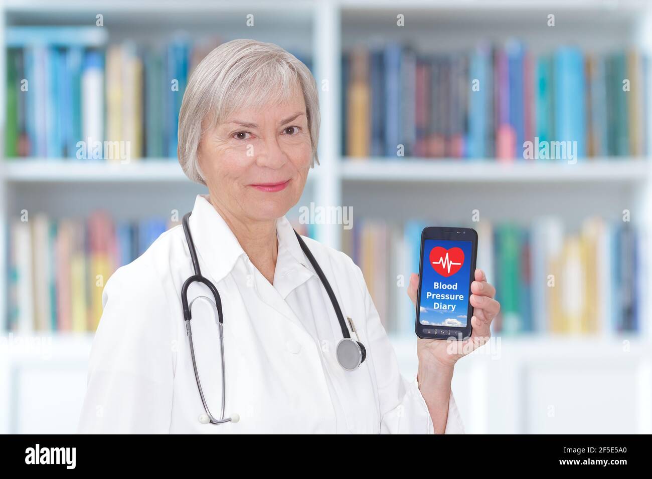 Friendly senior doctor with a smartphone showing a blood pressure diary app, mobile health concept. Stock Photo