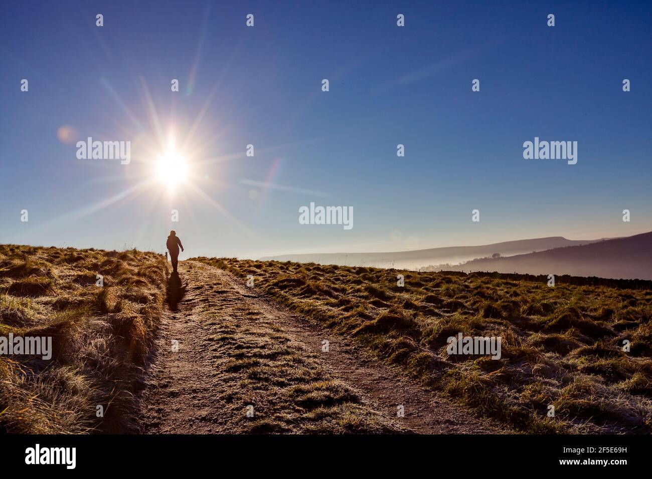 Woman silhouetted against the bright sun walking on a track in the High Peak, Derbyshire, UK Stock Photo