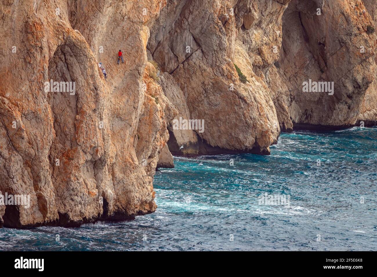 Tiny rock climbers on the huge red seacliffs of Toix at Calpe, Costa Blanca, Spain Stock Photo