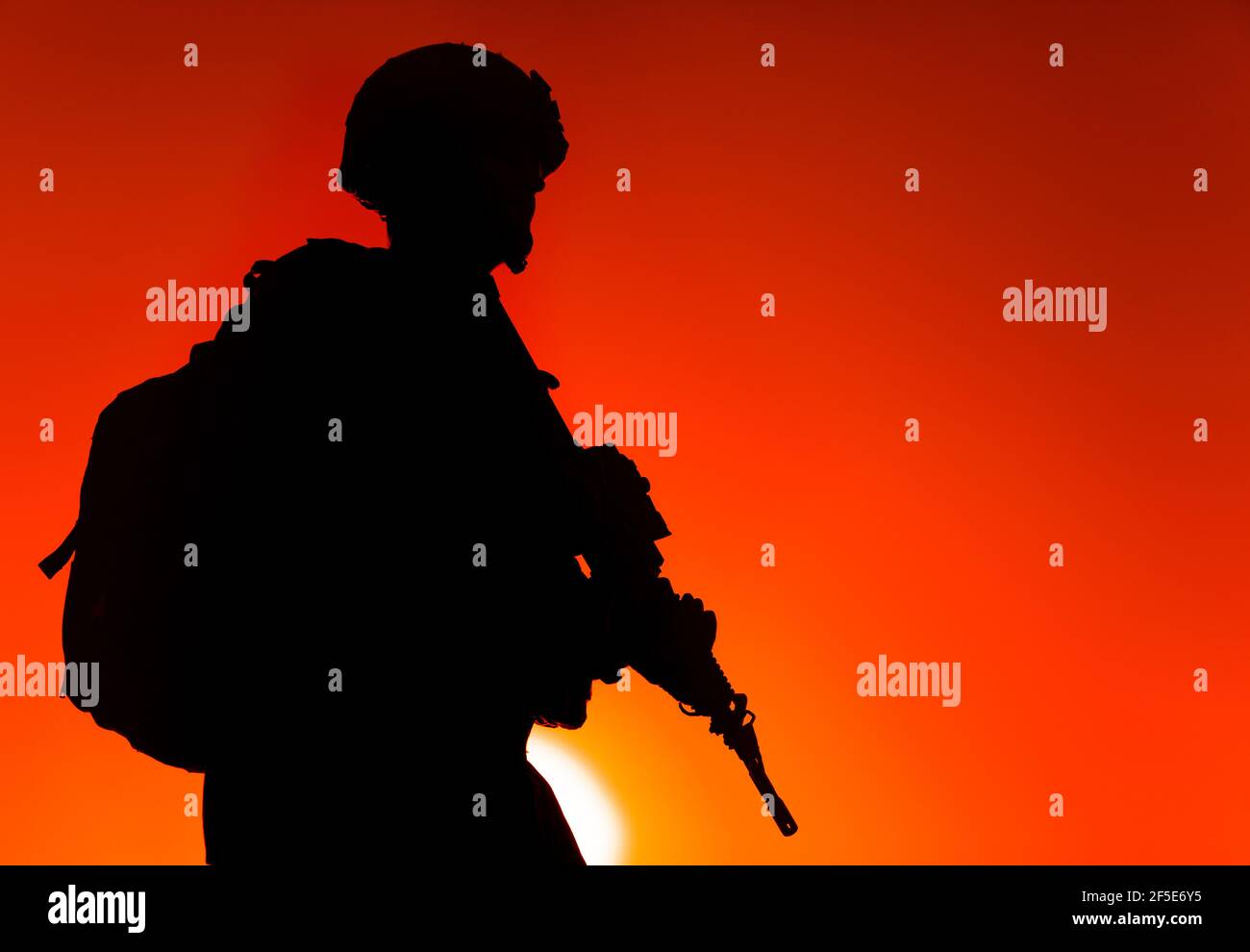 Silhouette of army rifleman in helmet and ammunition, carrying tactical backpack, walking with service rifle on background of sunset sky. Counter terrorist forces fighter marching at night mission Stock Photo