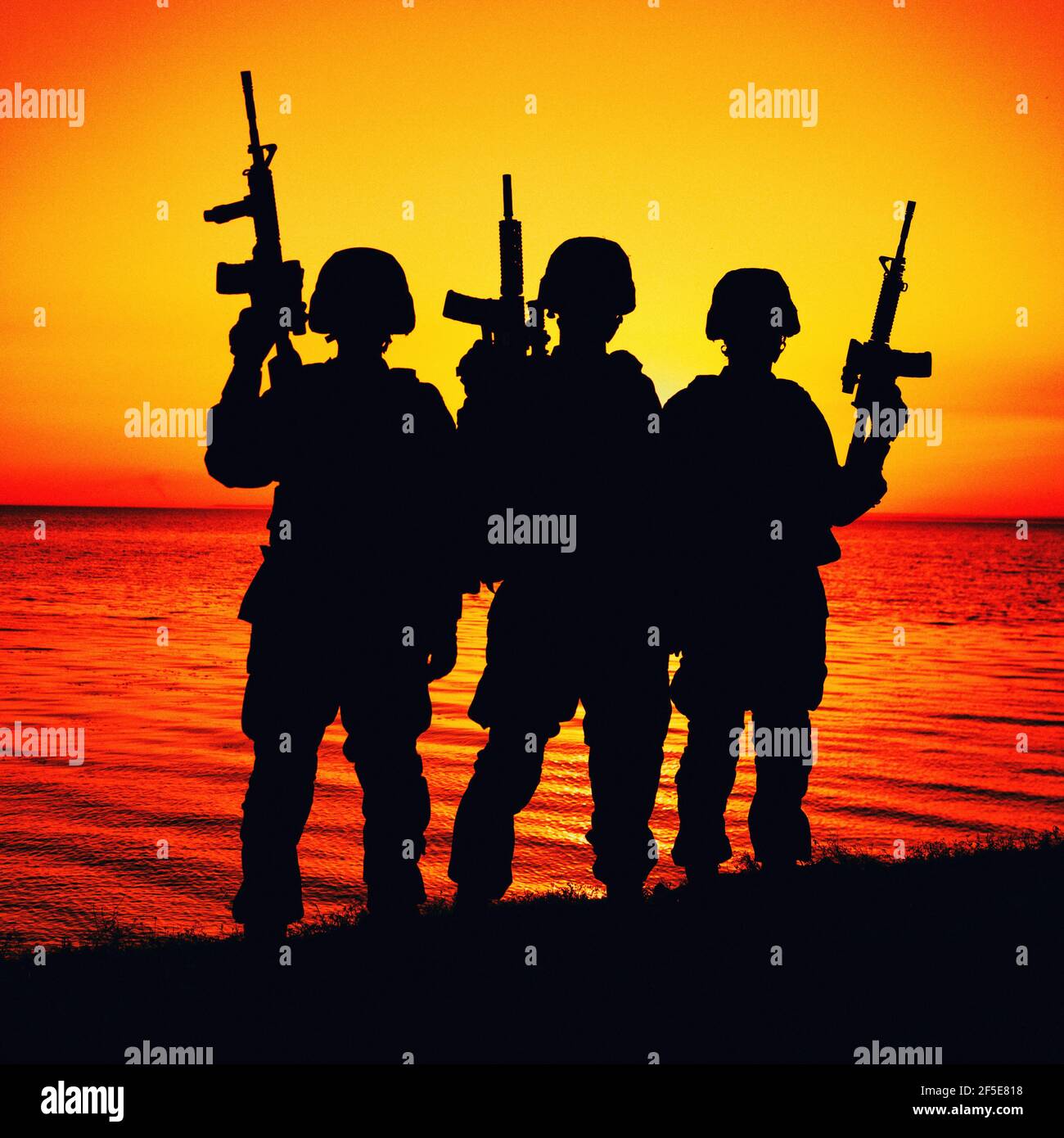 Silhouette of army special operations forces soldiers team, group of Marines or coast guard fighters crew in ammunition and combat helmets standing on seashore at sunset with raised assault rifles Stock Photo