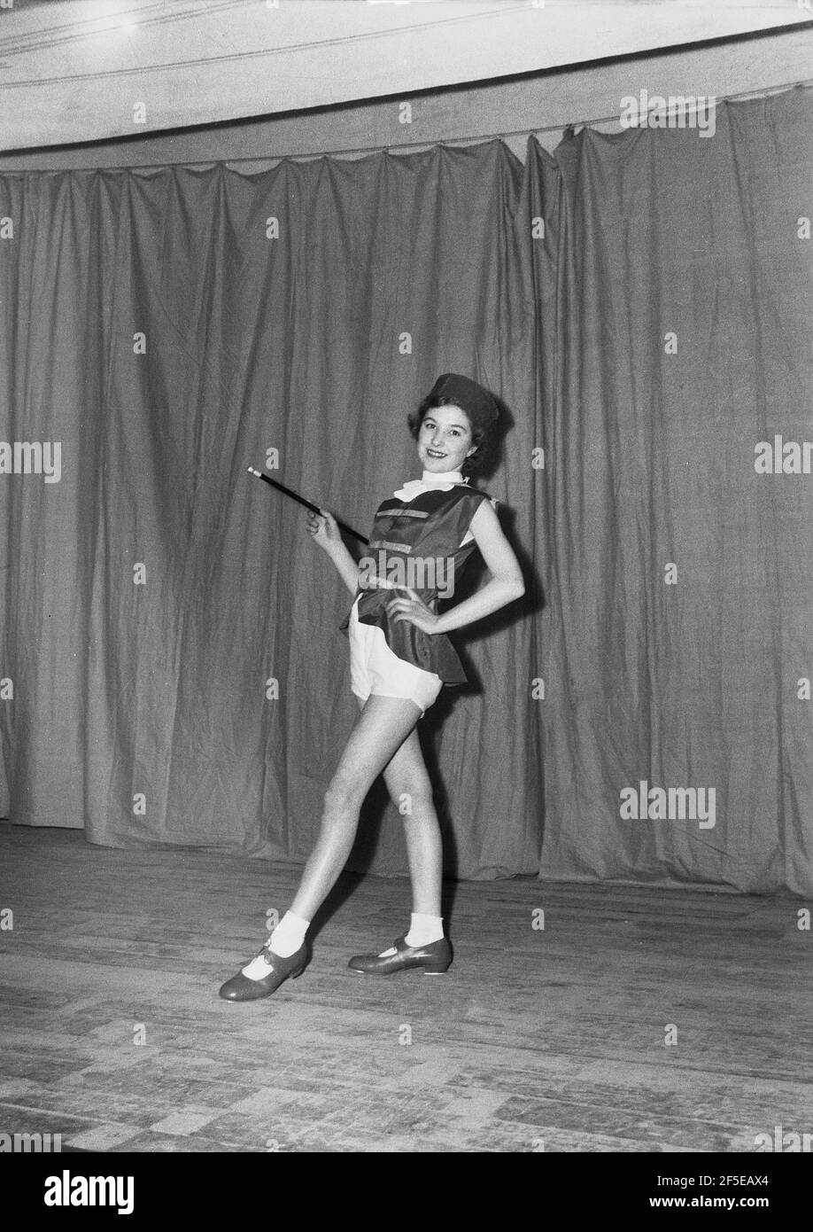 1954, historical, on a stage infront of the curtain wearing her costume and with baton, a young female dancer posing for a photo before performing in the pantomime, 'Mother Goose', England, UK. Originally the imaginary author of a collection of French fairy tales and later of popular English nursery rhymes, it is said that the character first appeared in 1806 as the performance, 'Harlequin and Mother Goose or The Golden Egg'. Different pantomime adaptions of the Mother Goose story took place in the 19th and 20th centuries and it has remained a popular family entertainment show ever since. Stock Photo